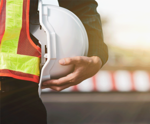 construction worker wearing reflective vest holds white hard hat
